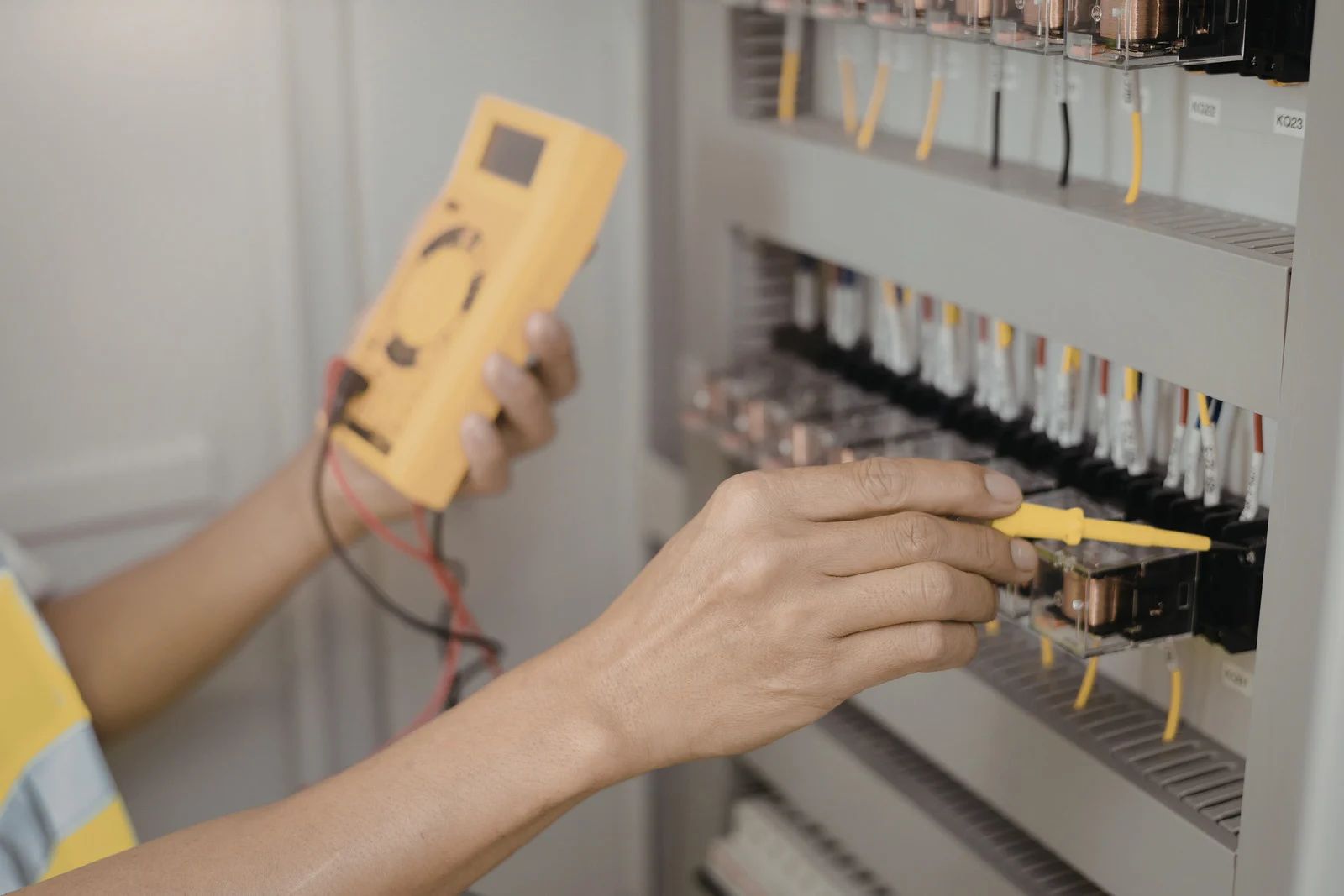 Electrician testing wires in electrical panel with a yellow multimeter.