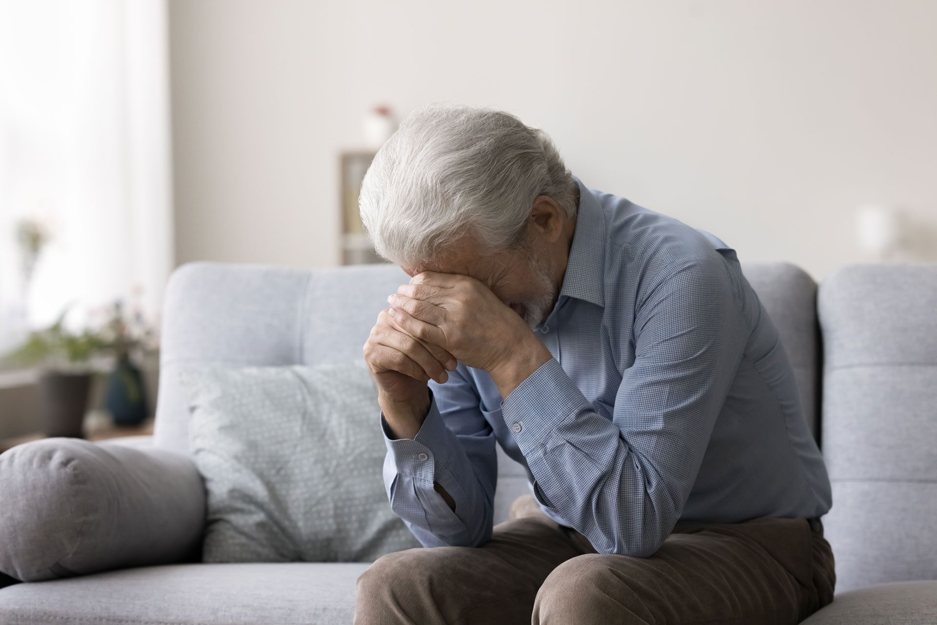 A person sits on a sofa with their head in their hands, expressing distress or grief.