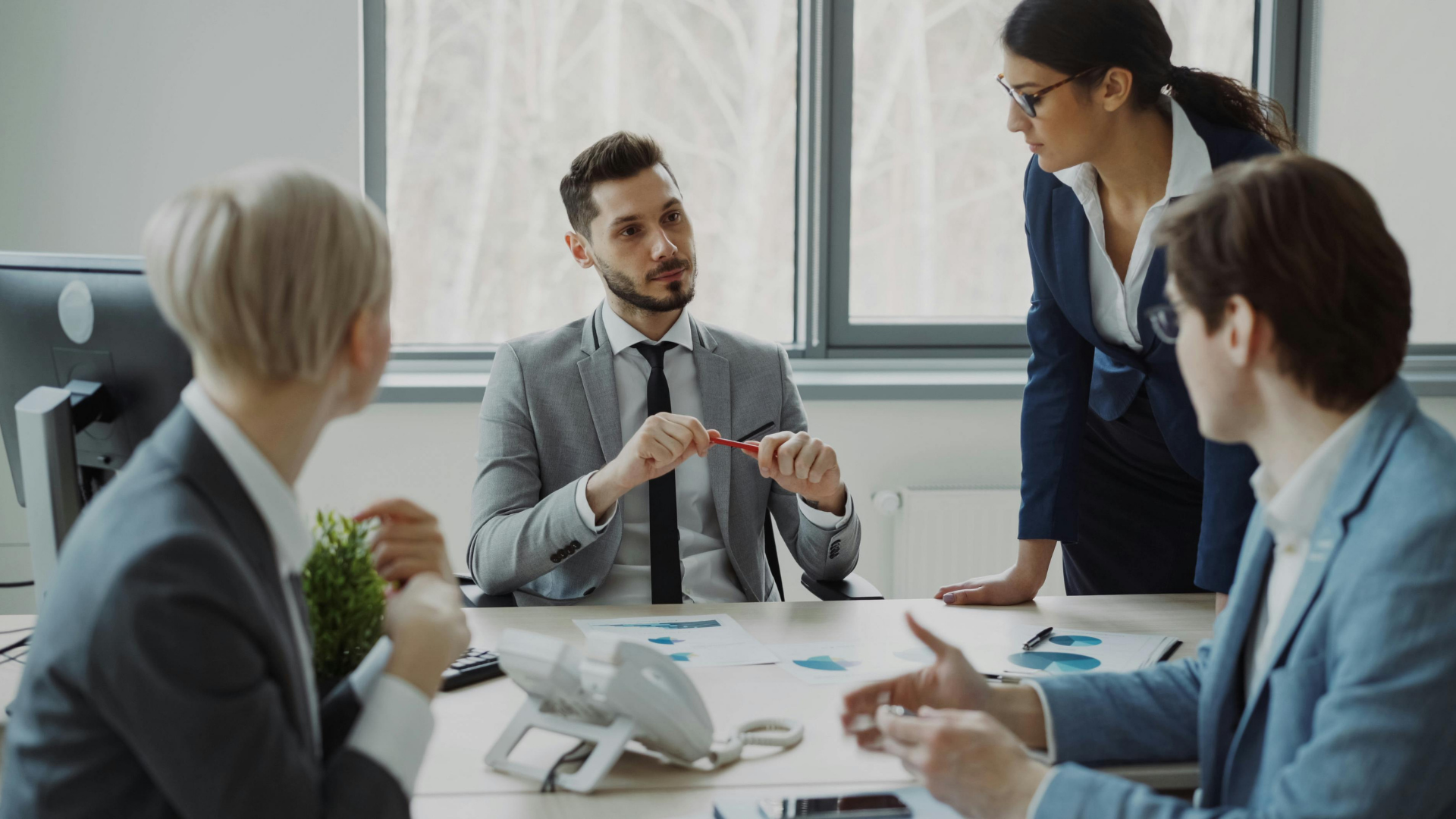 Business meeting with four coworkers discussing documents around a conference table in a bright office