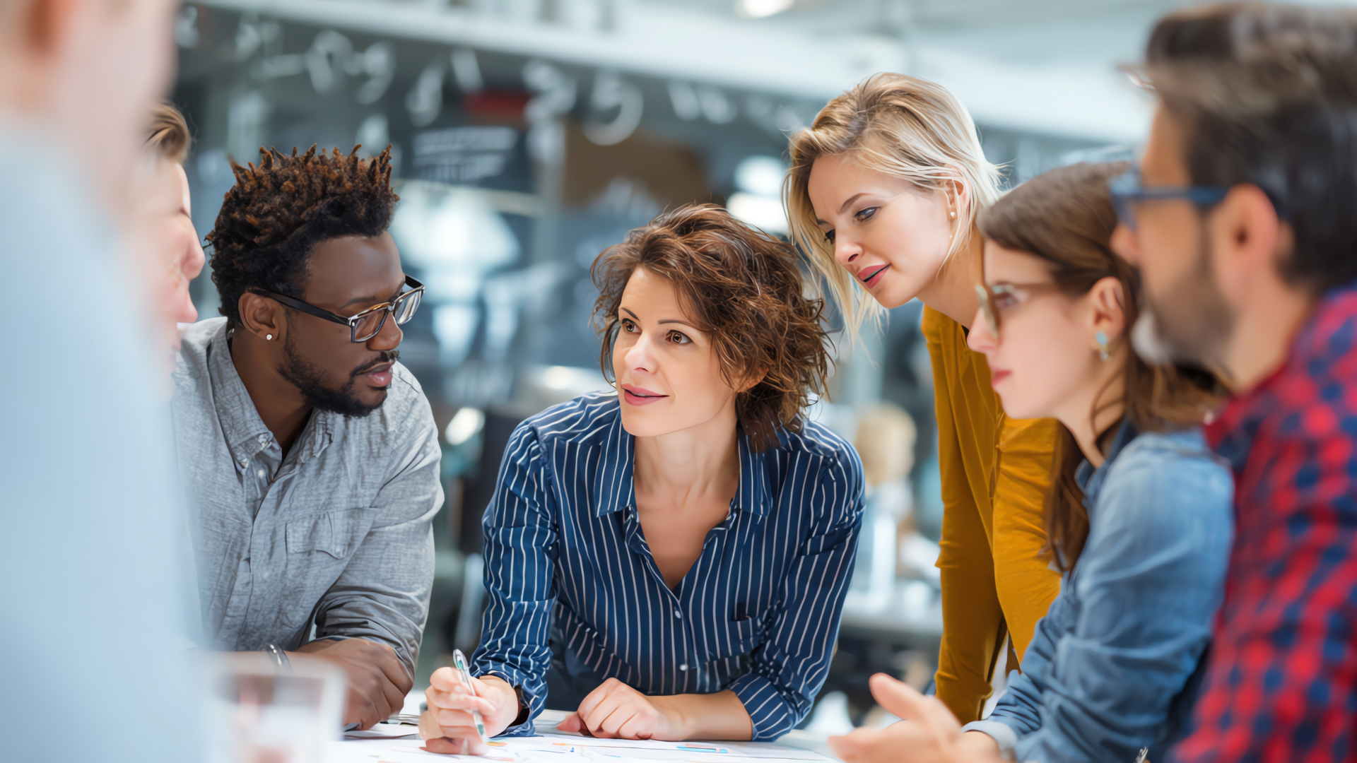 Small group in a meeting, leaning over documents and discussing ideas around a table.