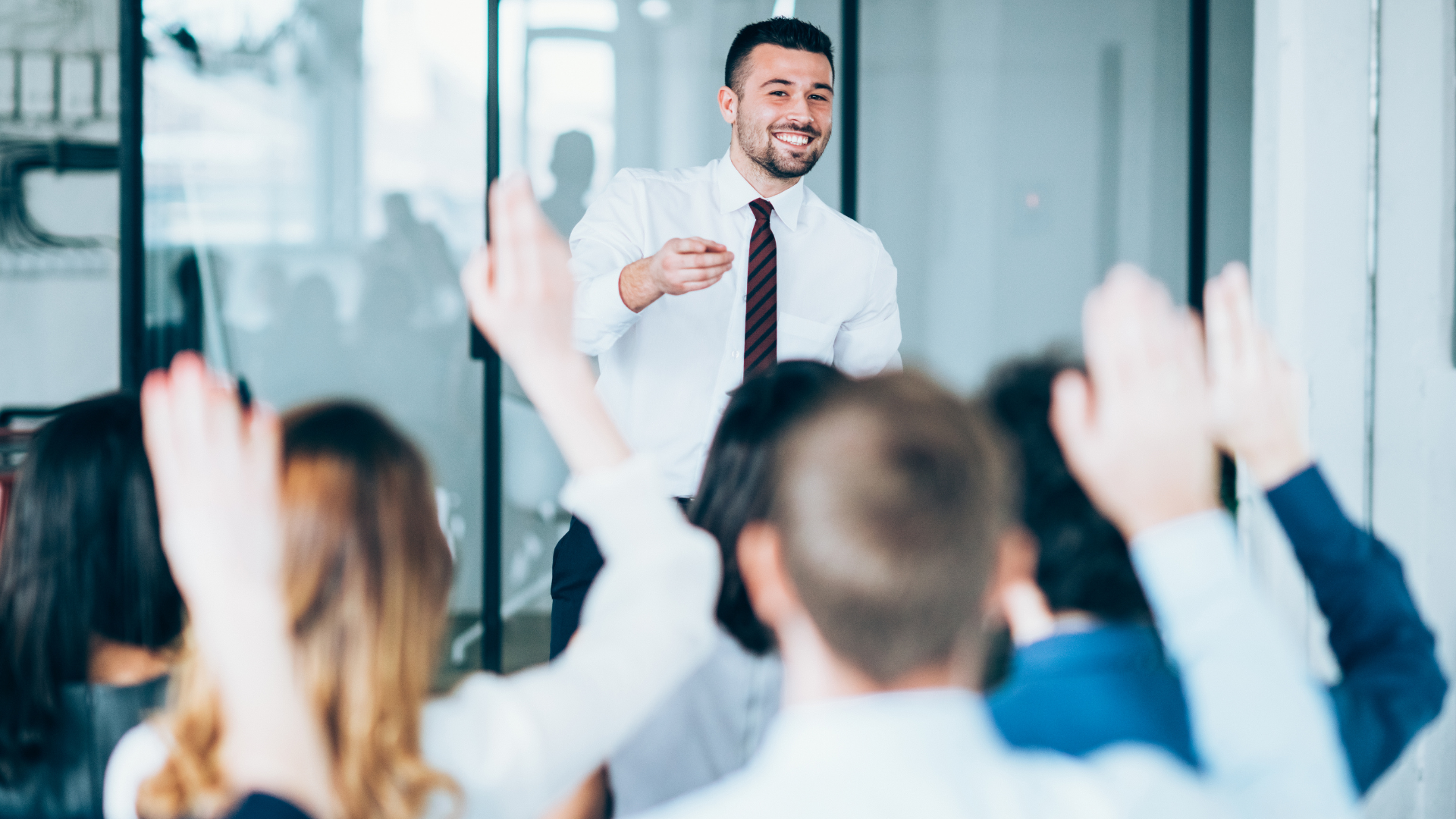 Presenter speaking to an engaged audience in a bright office meeting room, with hands raised in front.