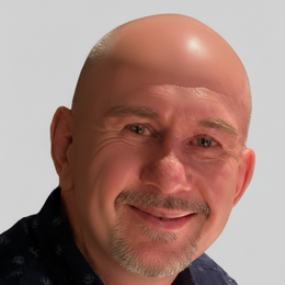Bald man with a slight smile, wearing a dark blue shirt; gray background.