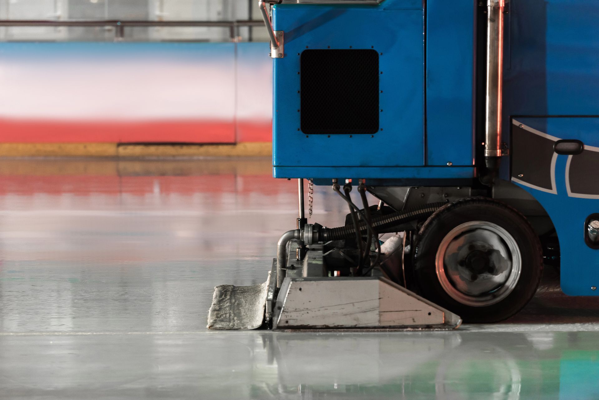 Una macchina blu per la levigatura del ghiaccio uniforma la superficie ghiacciata all'interno di una pista di pattinaggio al coperto.