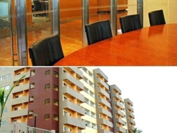 Una vista a schermo diviso: una moderna sala riunioni con tavolo in legno e sedie nere sopra un condominio a più piani.