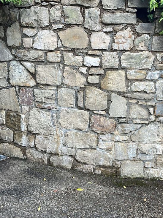 Un muro dalla texture particolare, realizzato con pietre naturali di colore grigio chiaro e beige, sovrapposte e di forma irregolare.