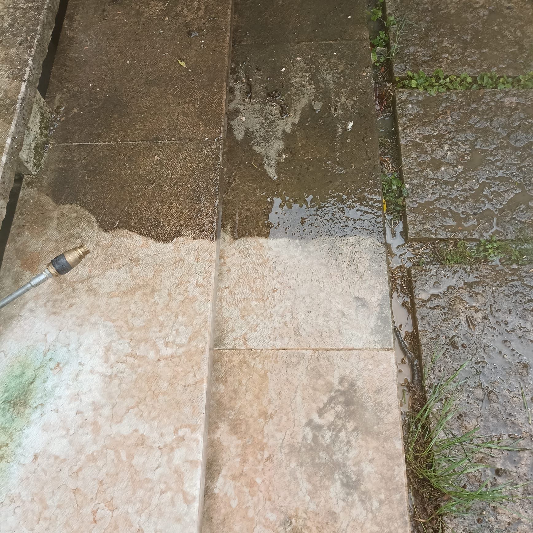 L'ugello di un'idropulitrice pulisce un patio in pietra sporco e scuro, rivelando una superficie sottostante più chiara e luminosa.