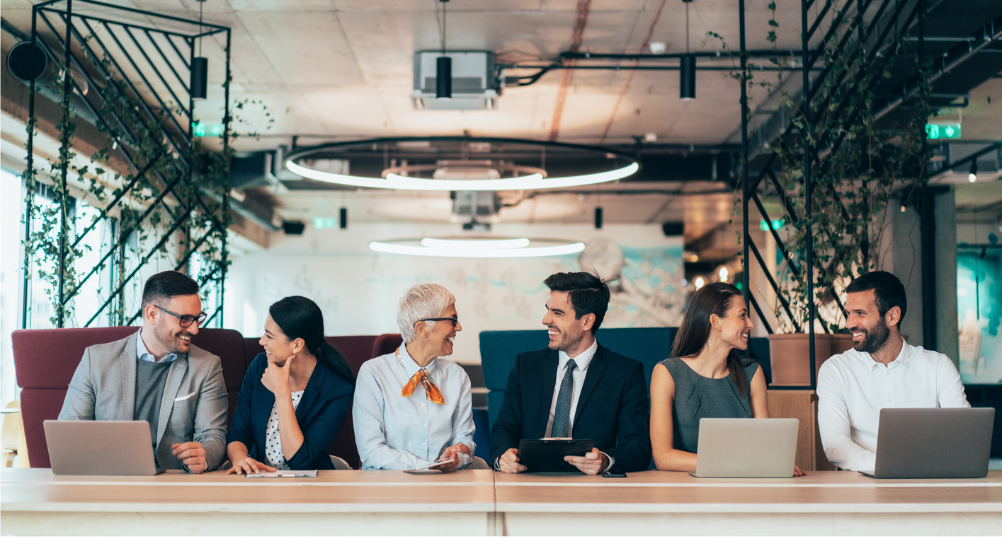 Business colleagues in an office, diverse group smiling at each other, working on laptops.