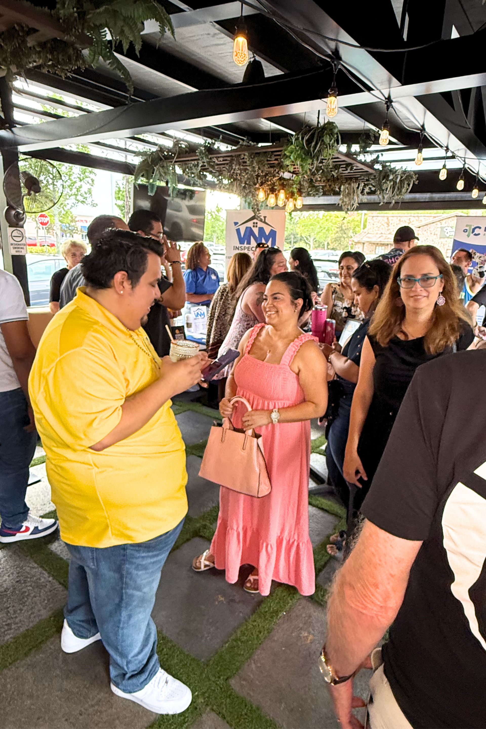 People gathered outdoors, man in yellow shirt showing something to a woman in a pink dress; others watch nearby.