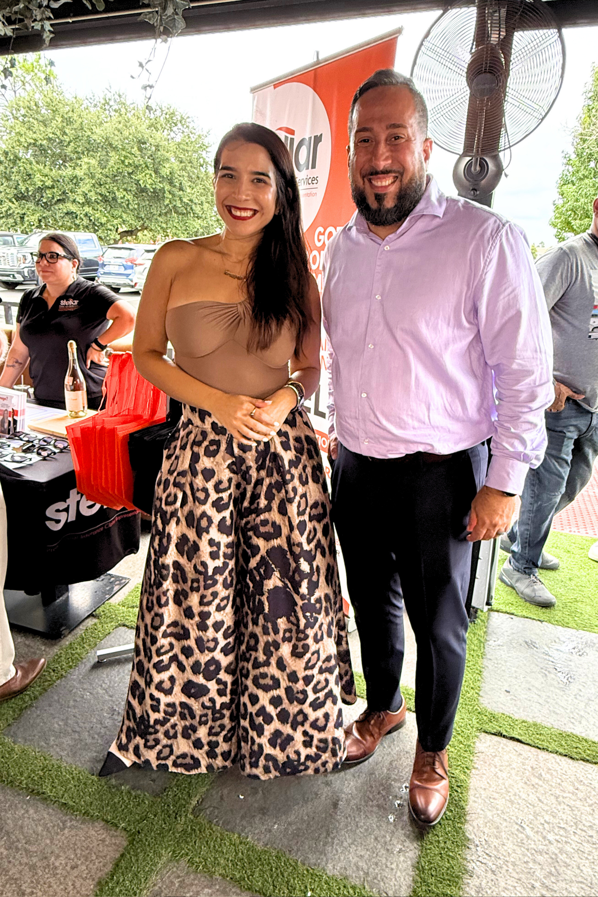 Woman in leopard print pants and man in purple shirt pose outdoors, smiling.