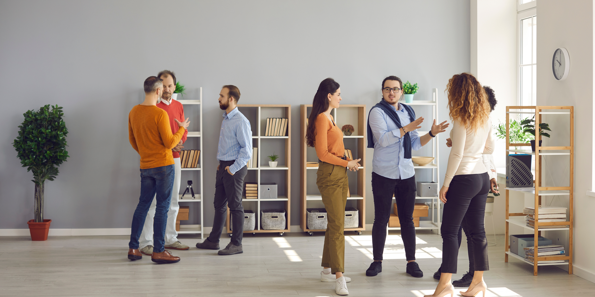 People in an office socializing. Three men in the left side; two women and two men in the right side.