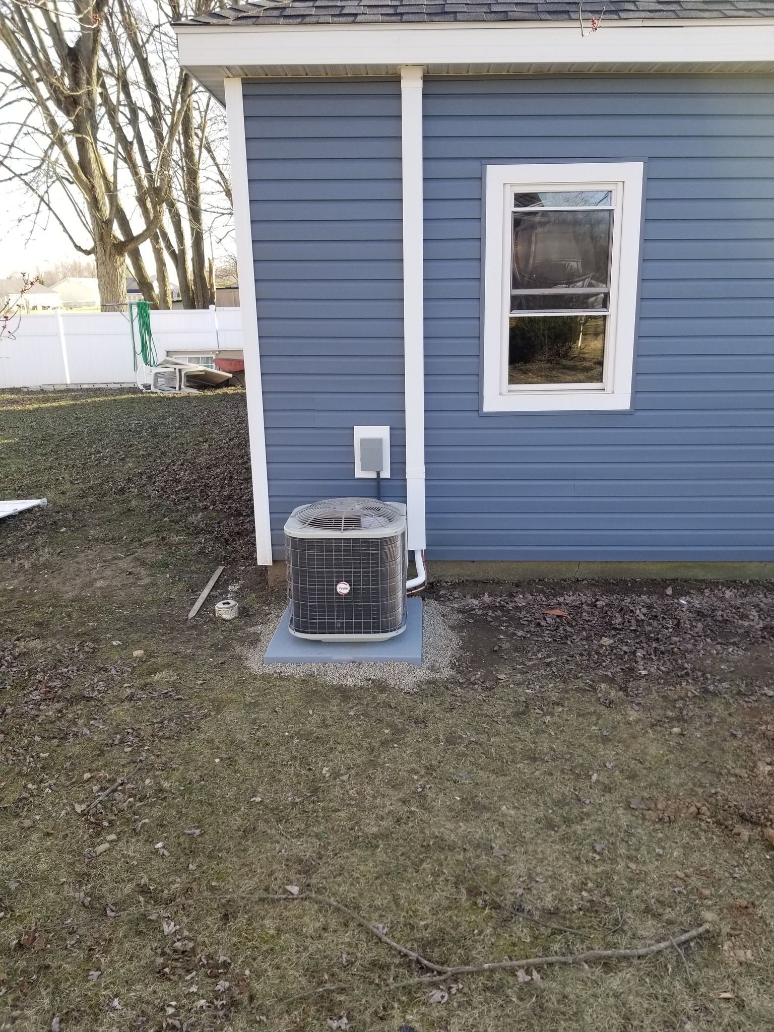 A blue house with white trim features a central air conditioning unit sitting on a concrete pad in the yard.