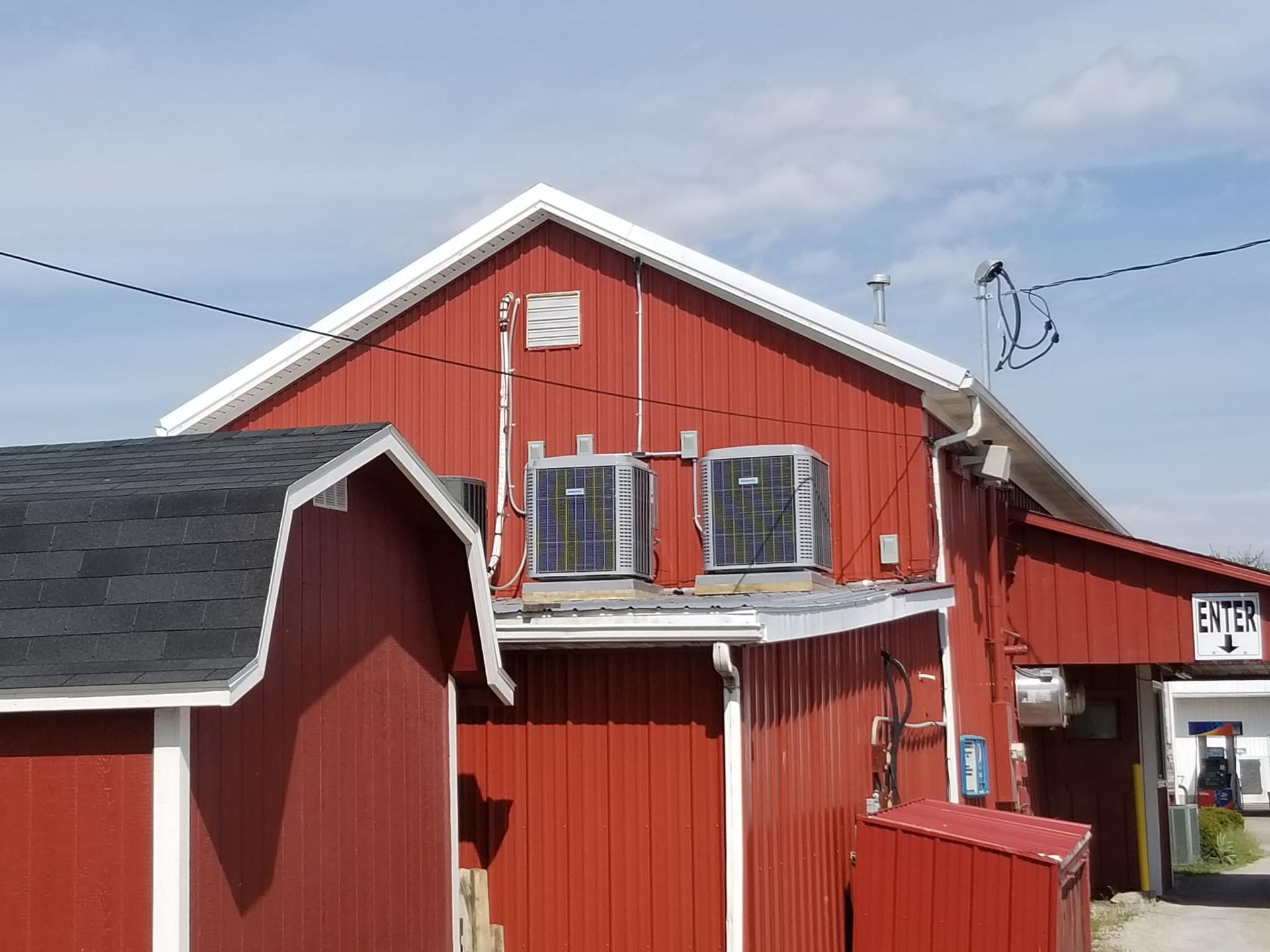 A red barn-style building with two outdoor air conditioning units mounted on its exterior wall under a blue sky.