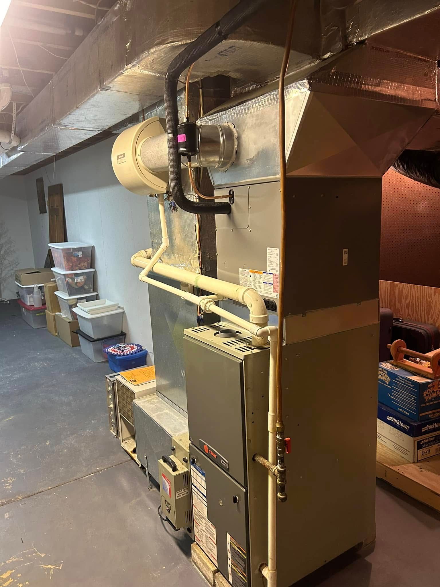 A beige residential furnace unit with connected metal ductwork in a basement storage area.