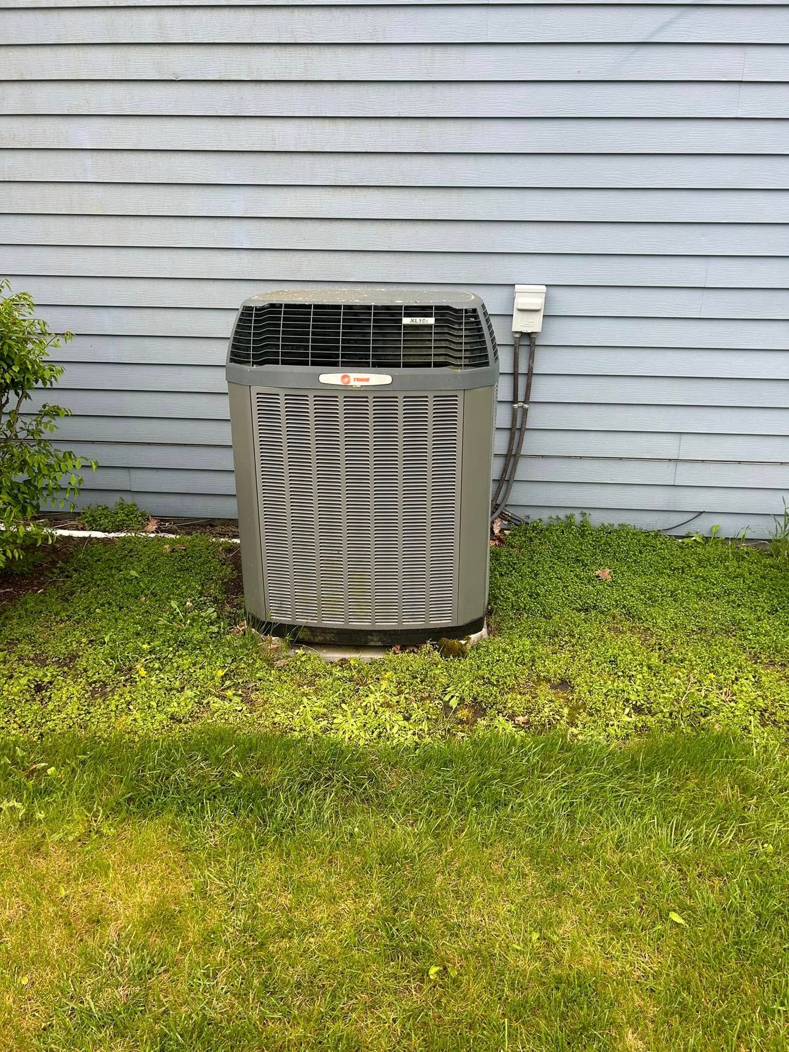 An outdoor central air conditioning unit sits on the grass against a house with light blue horizontal siding.