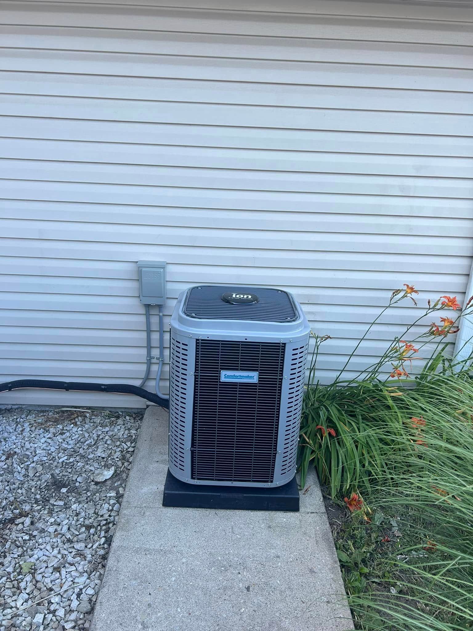 A grey, rectangular air conditioning unit sitting on a concrete pad against a house with light-colored siding.