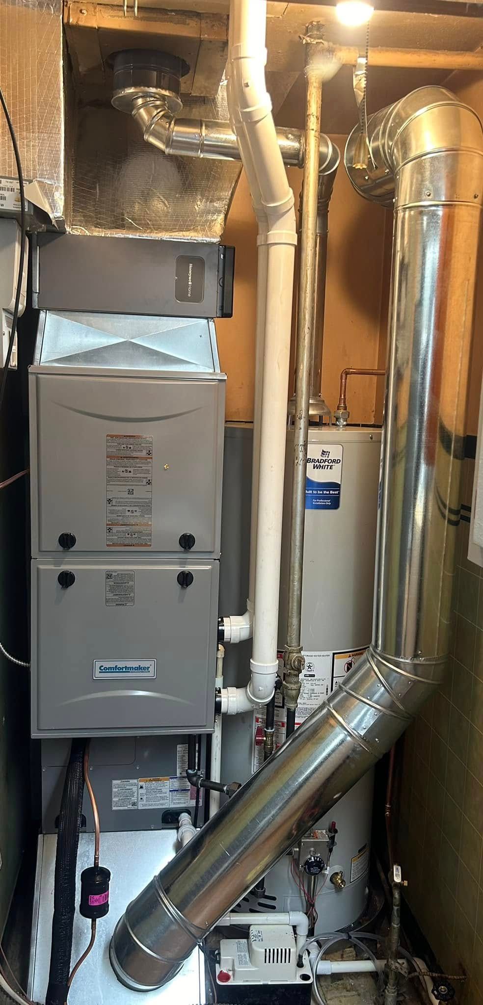A furnace and water heater system with metal vent piping and white PVC pipes in a utility closet.