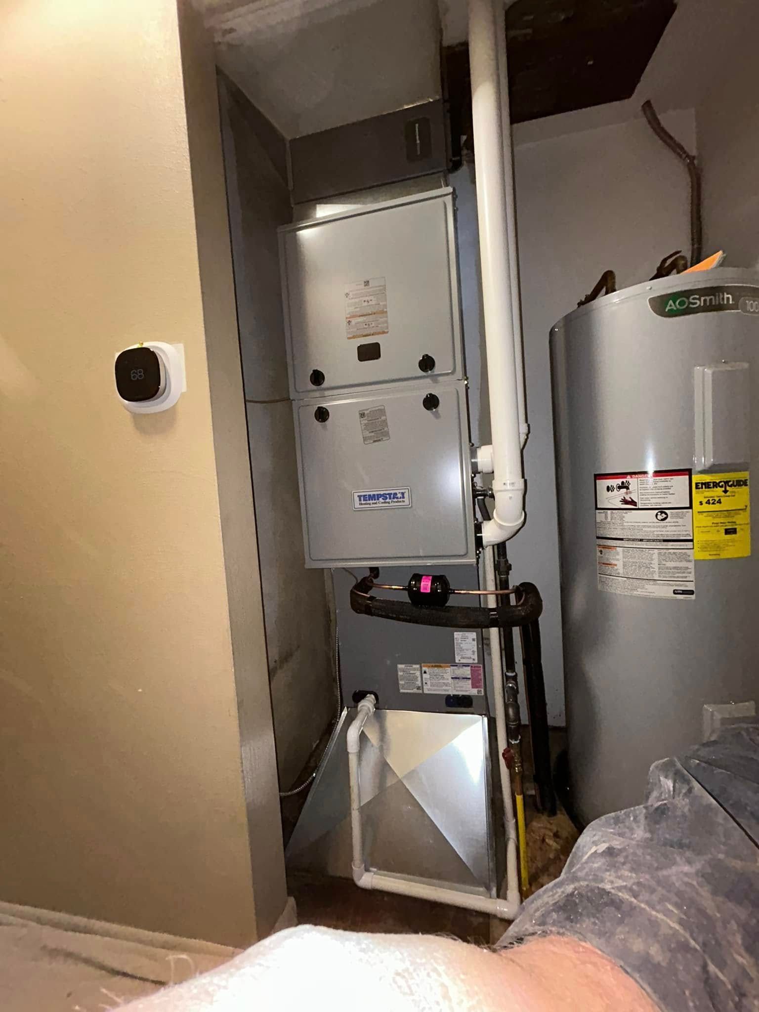 A tall metal furnace unit and a silver water heater standing side-by-side in a utility closet.