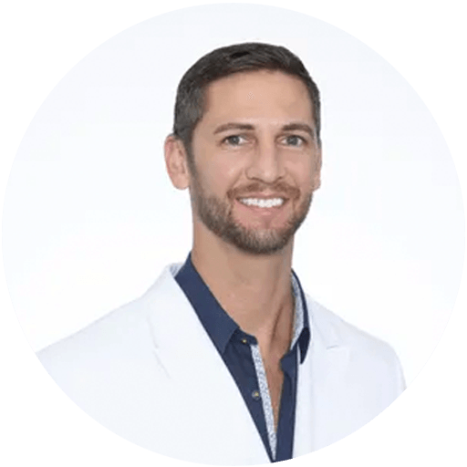A man with a beard is wearing a white lab coat and smiling.