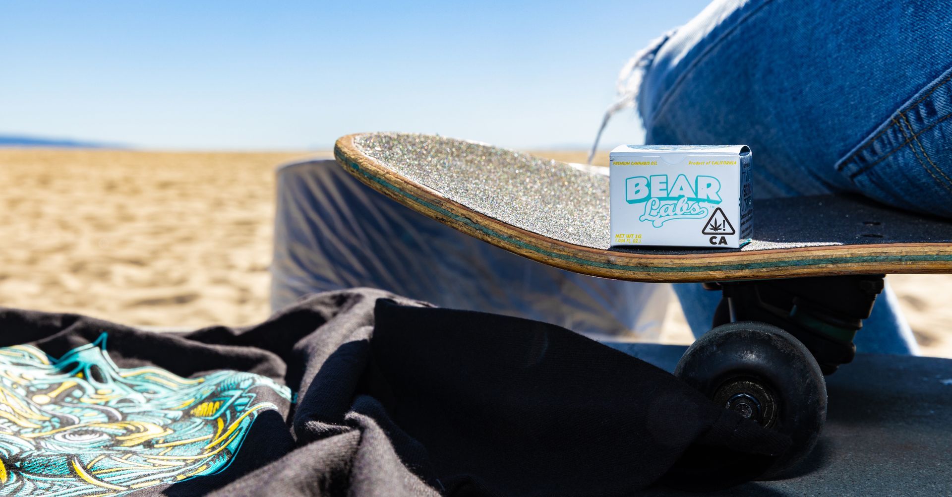 A person is sitting on a skateboard on the beach.