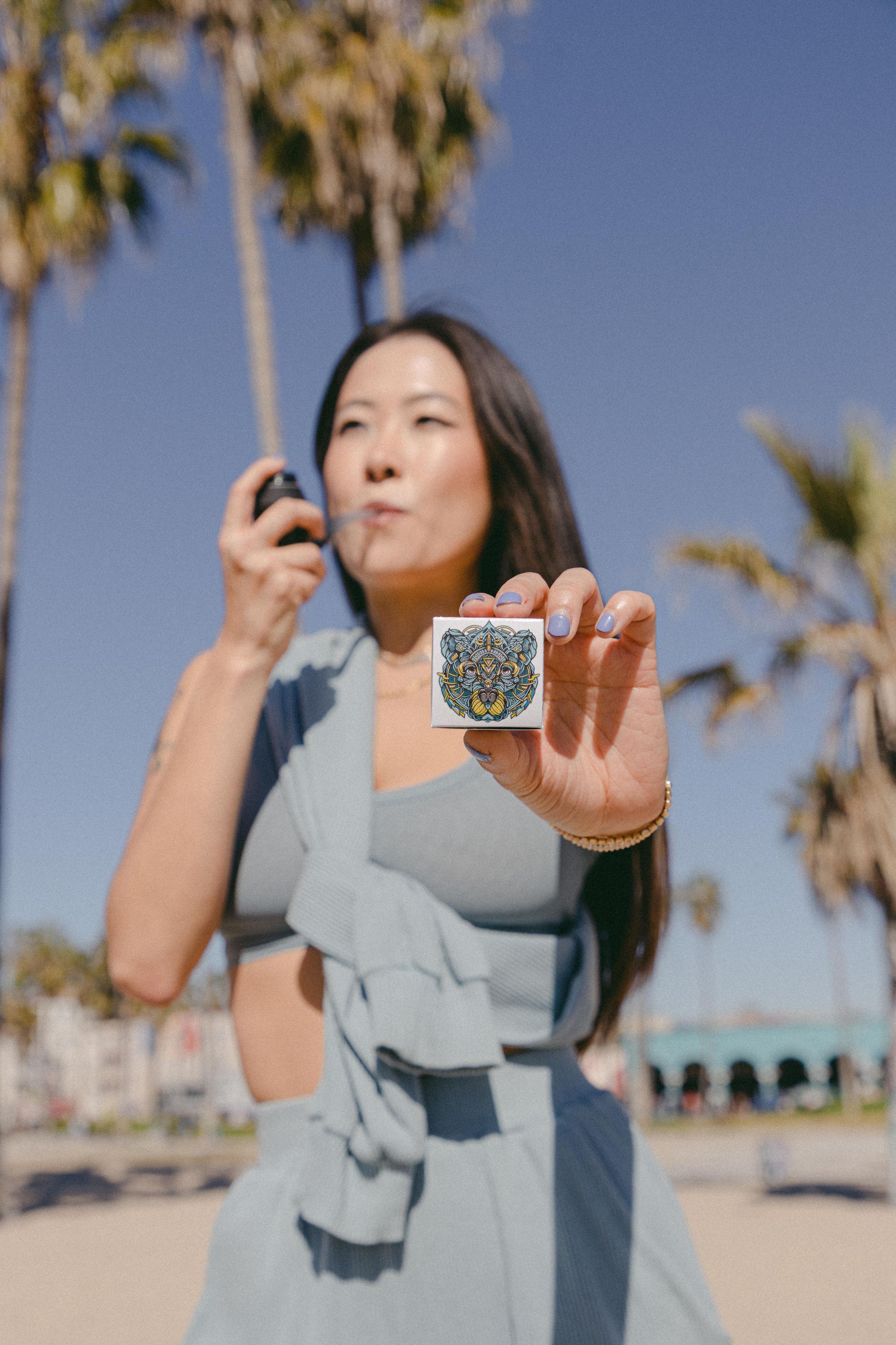 A woman in a blue dress is blowing soap bubbles on the beach.