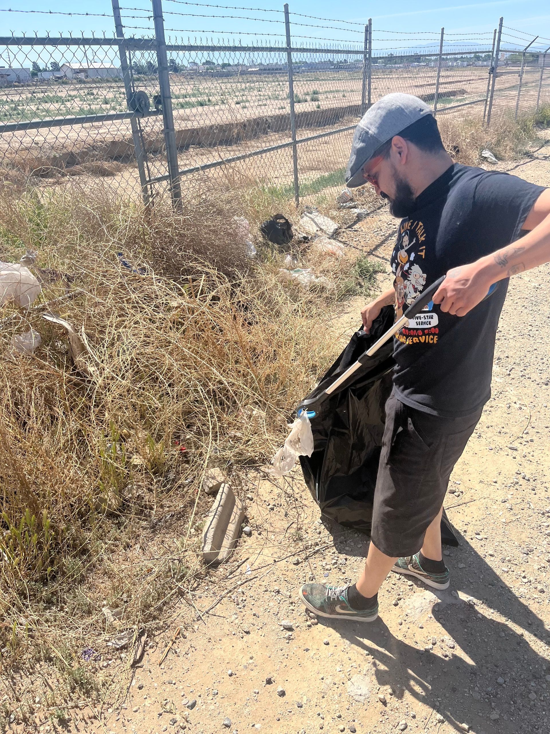 A man is picking up trash on the side of a dirt road.