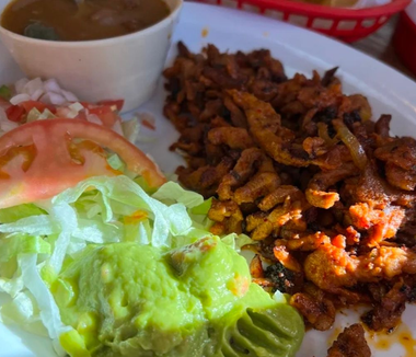 Plate of Mexican food with lettuce, avocado, tomato, rice, and seasoned meat, plus a small cup of sauce
