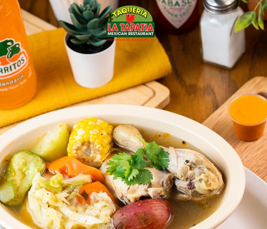 Bowl of colorful seafood soup with corn, potatoes, avocado and cilantro on a wooden table