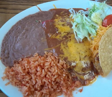 Plate with refried beans, red rice, enchiladas topped with melted cheese, lettuce, and tortilla chips