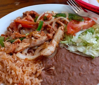 Plate of Mexican food with chicken fajitas, rice, refried beans, and lettuce salad