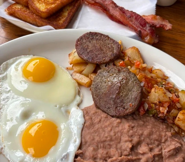 Breakfast plate with sunny-side-up eggs, sausage, refried beans, hash browns, and bacon