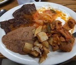 Plate of assorted cooked meats, beans, potatoes, and saucy vegetables on a white dish