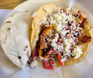 Plate with a cheese-topped taco and a folded flour tortilla on a white paper liner