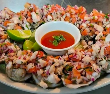 Seafood ceviche platter with lime wedges and red dipping sauce in a small bowl