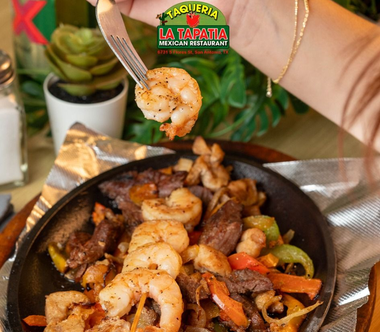 Shrimp and steak fajita skillet with peppers, onions, and a tortilla chip on a table