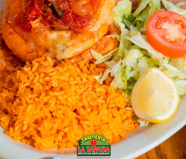 Plate of orange rice with chicken, lettuce, tomato, and a lemon wedge on a restaurant dish