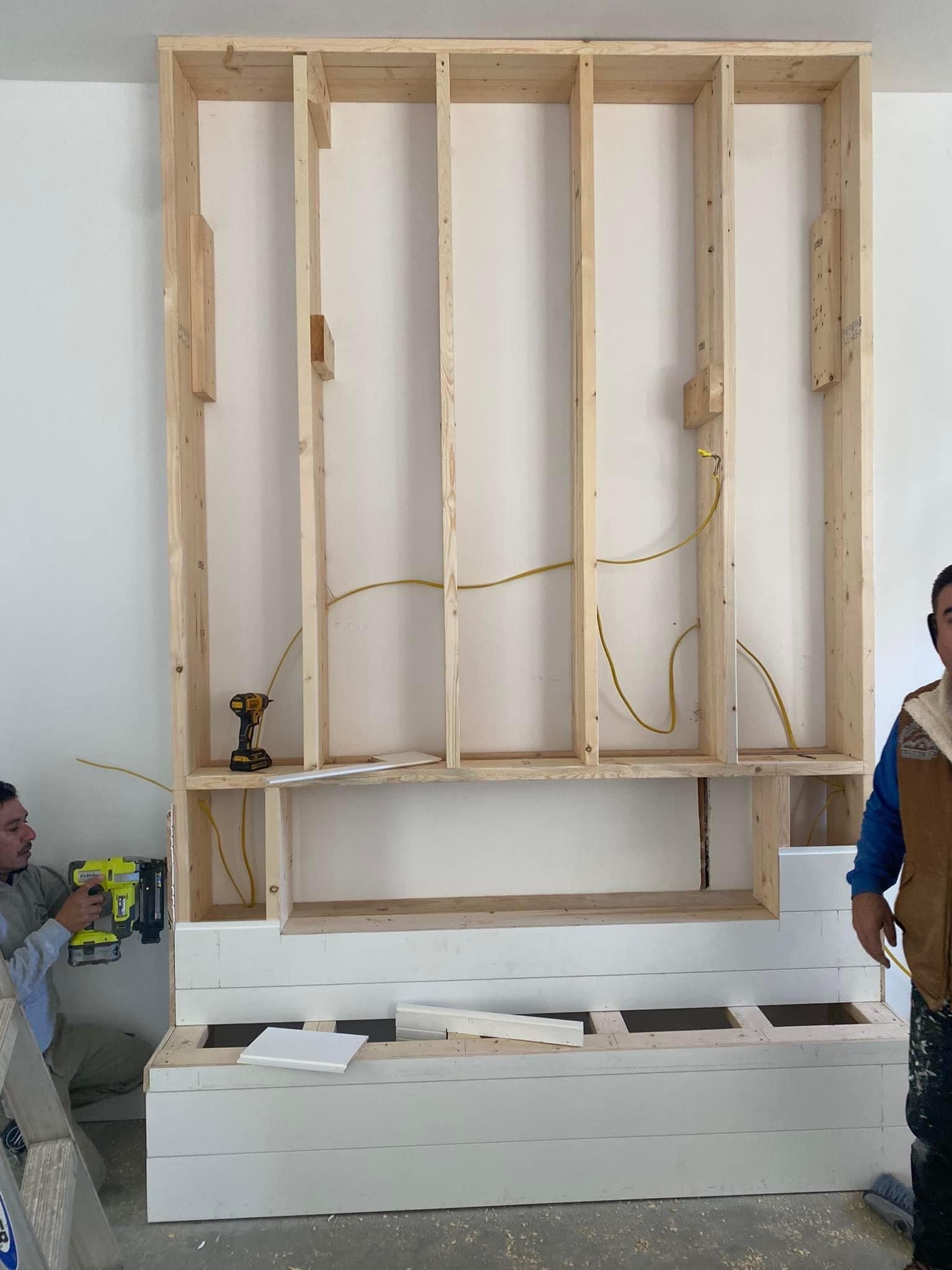 A man is standing in front of a wooden shelf that is being built.