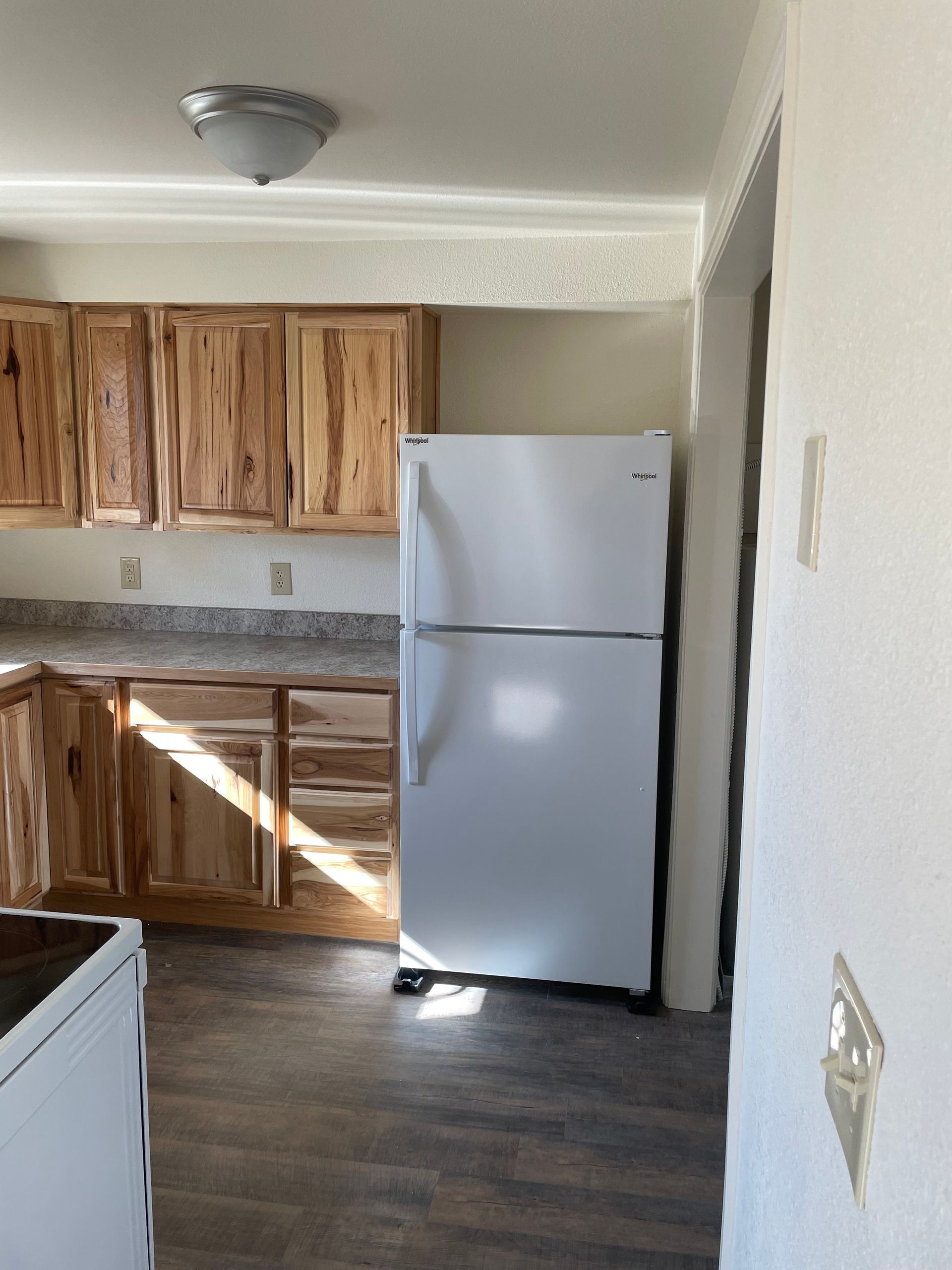 Kitchen with wooden cabinets, white refrigerator, and gray countertops. Dark wood-look flooring.