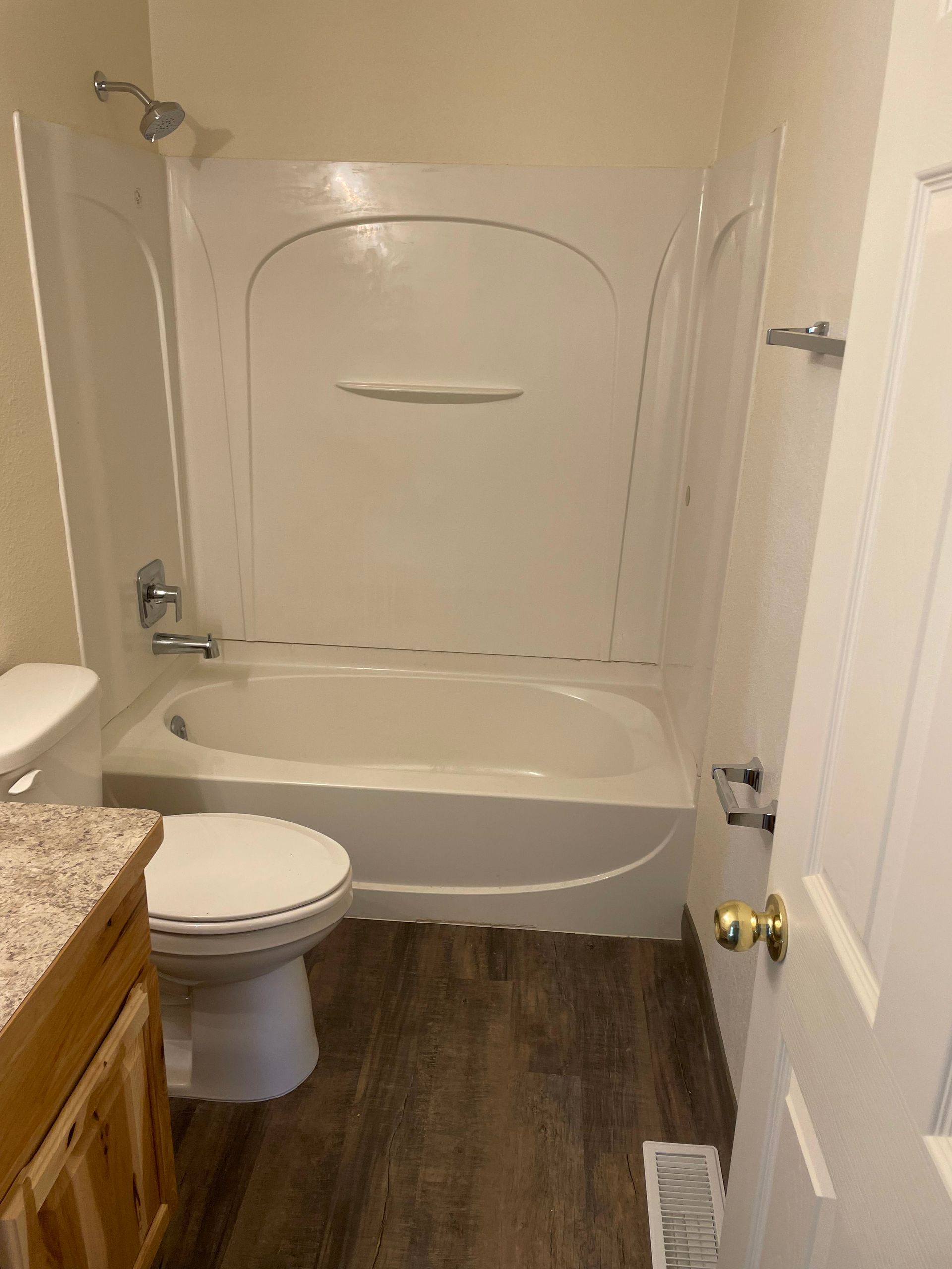 Bathroom with white tub/shower, toilet, vanity, and wood-look floor.