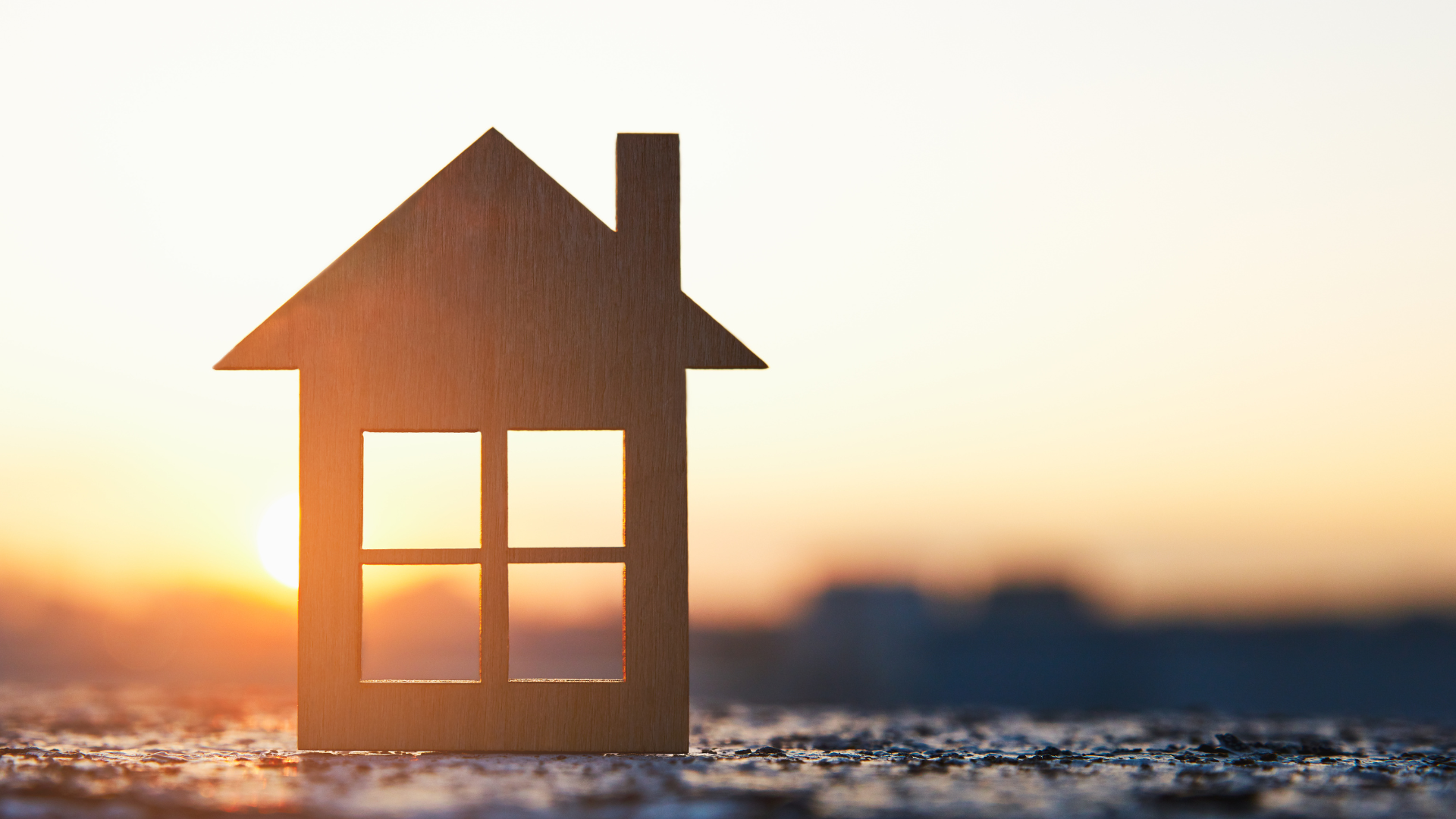 Silhouette of a house with chimney, in front of a bright sunset sky.
