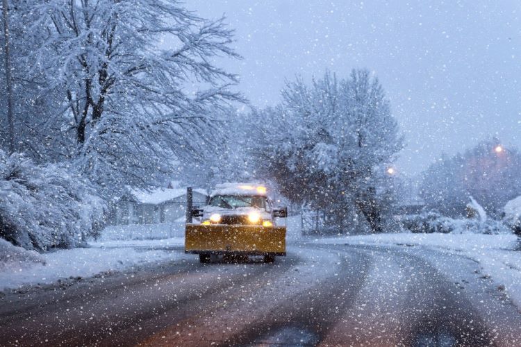 A snow plow is driving down a snow covered road.