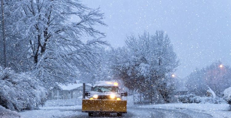 A snow plow is driving down a snowy street.
