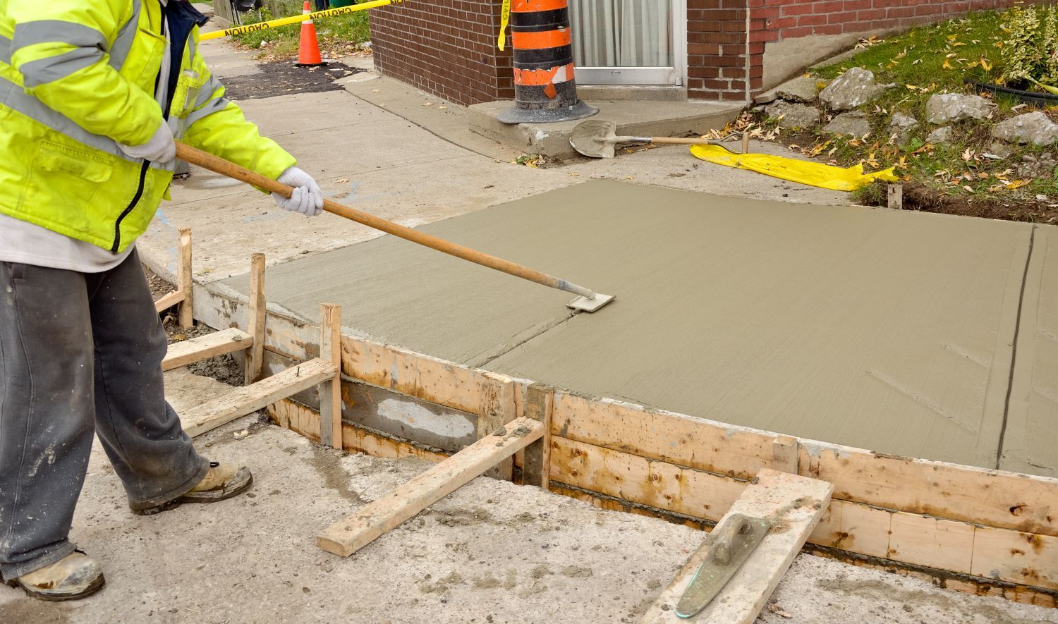 A man is spreading concrete on a sidewalk with a shovel.