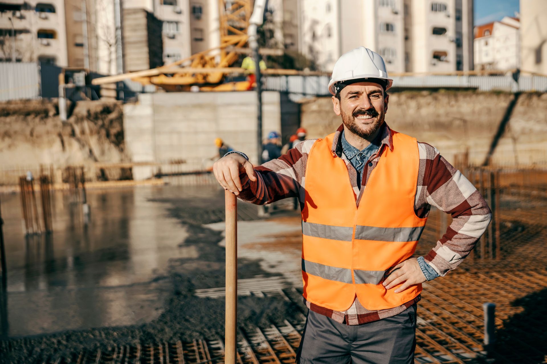 A construction worker is standing on a construction site holding a shovel.