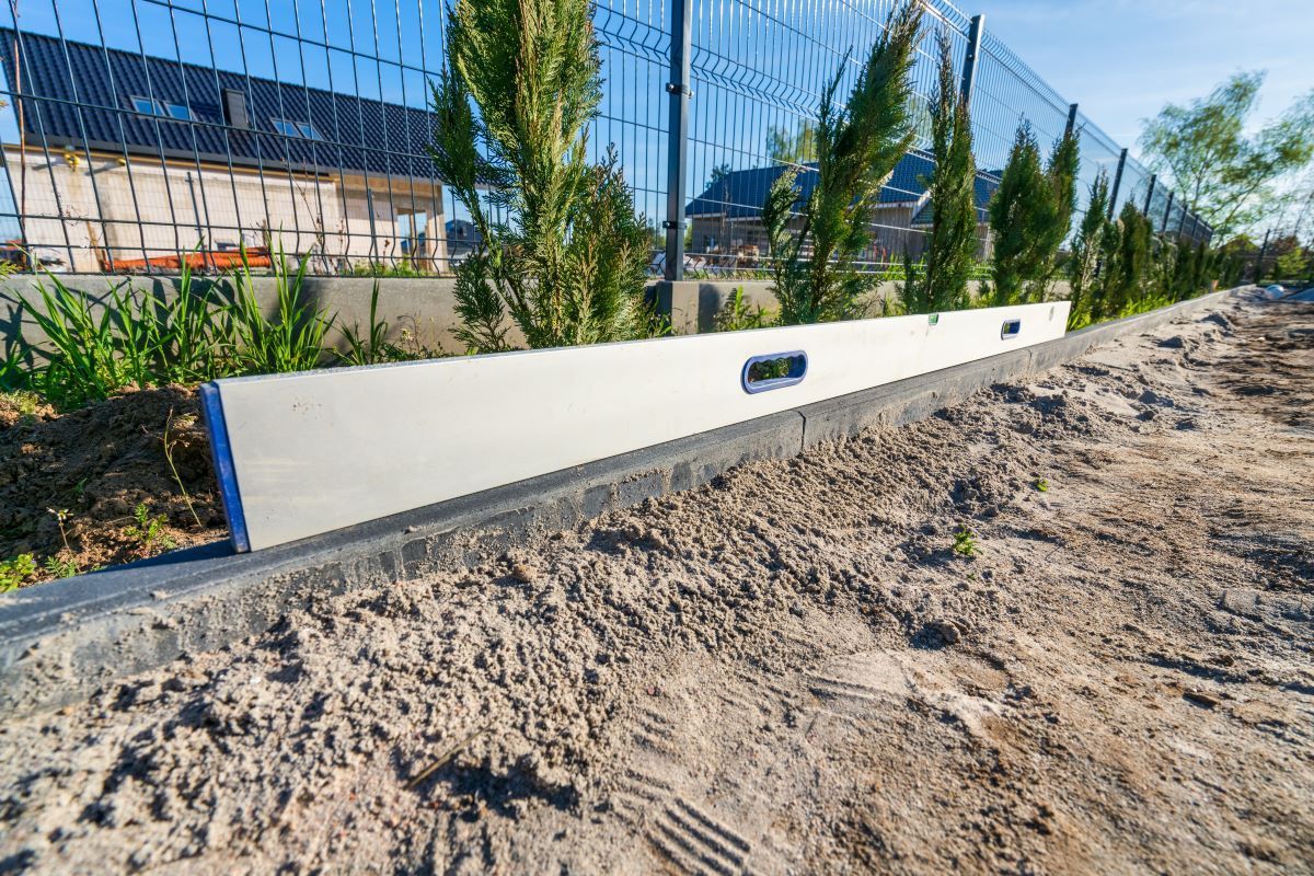 A white level is sitting on top of a dirt road next to a fence.