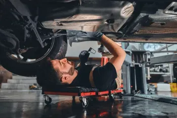 Mechanic lying on a creeper working under a car, in a garage | AutoHaus of Boulder