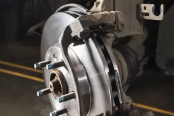 Close-up of a car's brake rotor and caliper, showing wear and tear | AutoHaus of Boulder