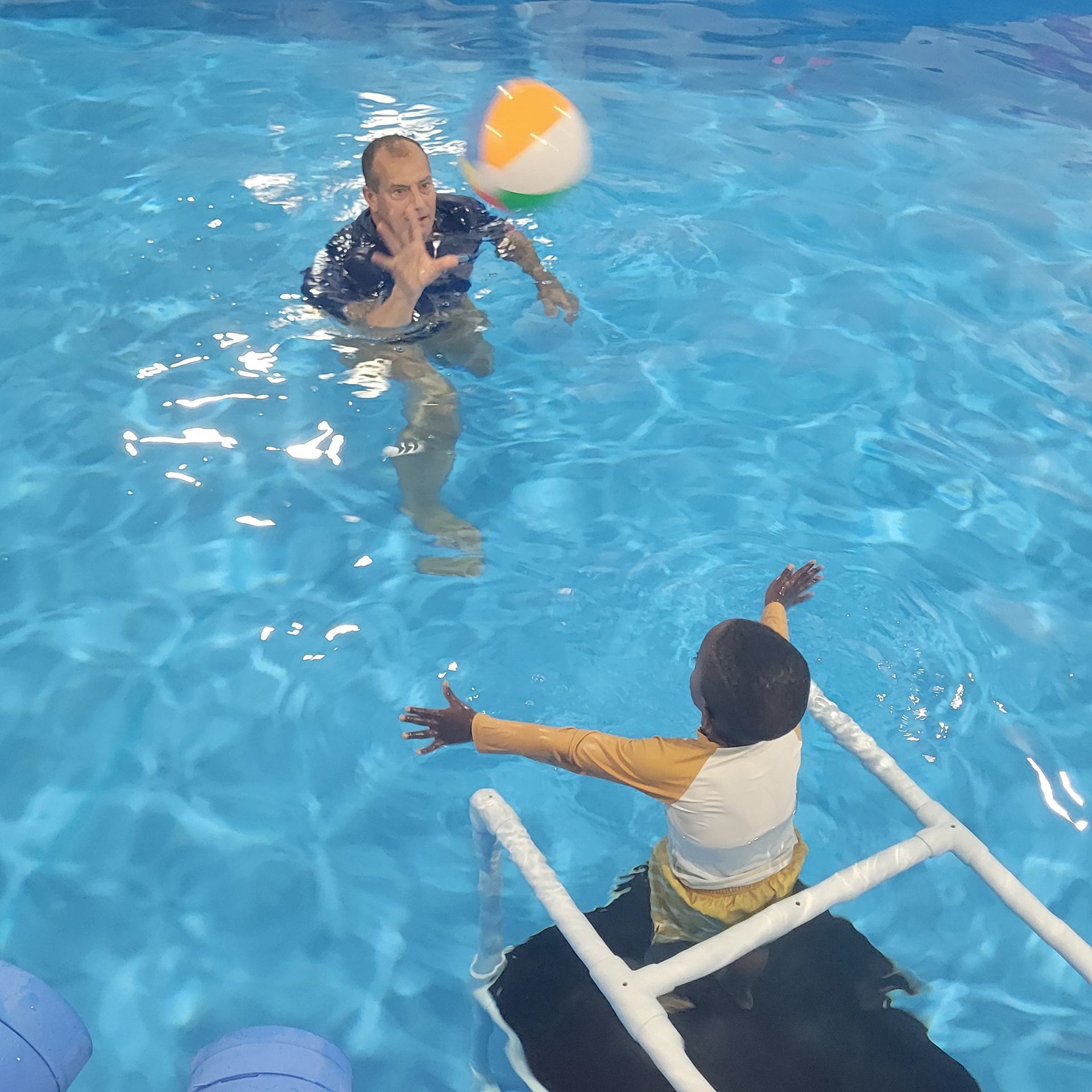 A man and a child are playing with a beach ball in a pool