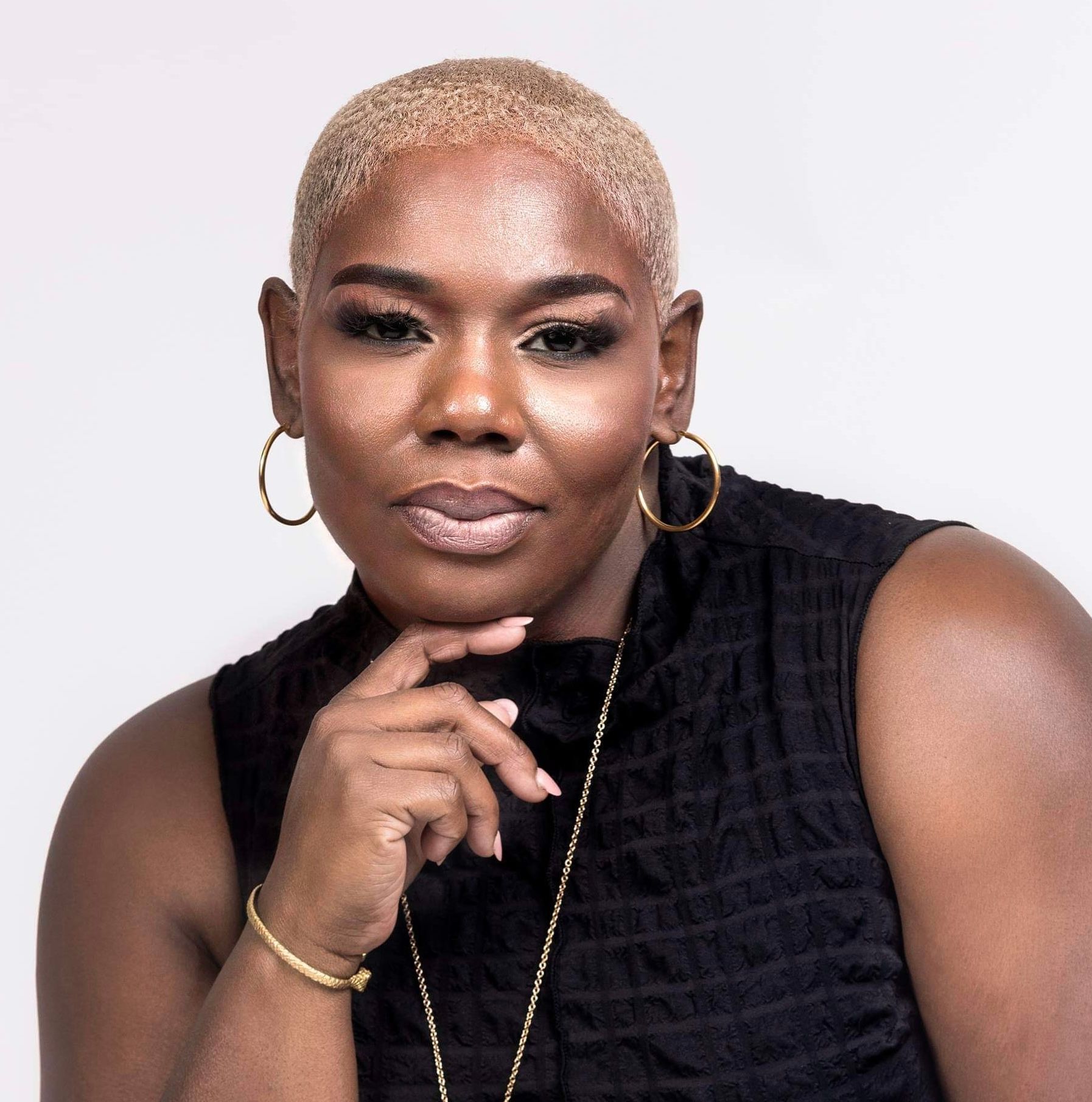 A woman with short blonde hair is wearing a black tank top and gold hoop earrings.