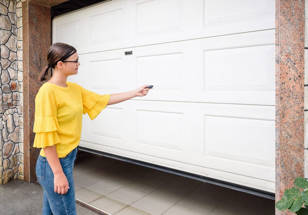A Woman In A Yellow Shirt Is Using A Remote Control To Open A Garage Door — Lighthouse Beach Garage Door Service in Port Macquarie, NSW