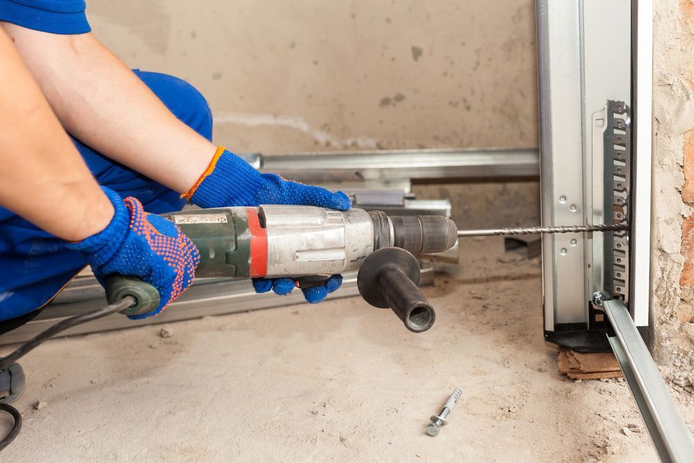 A Man Is Using A Drill Machine To Fix A Garage Door — Lighthouse Beach Garage Door Service in Bonny Hills, NSW
